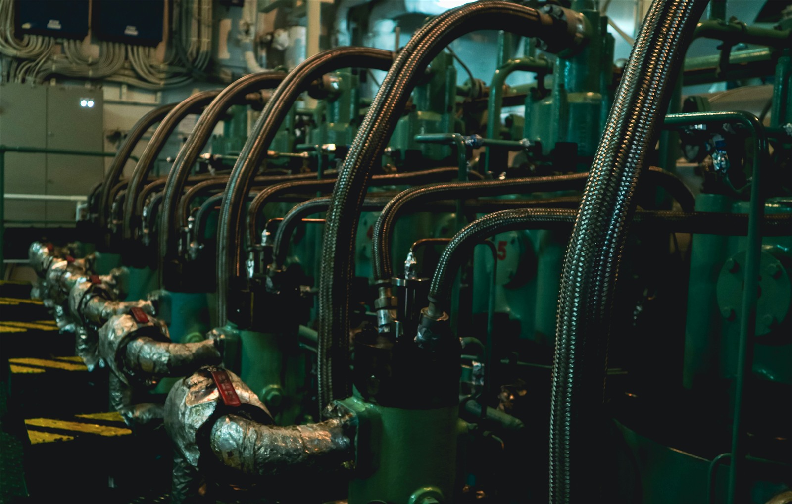 Engine room aboard a vessel, rows of engine blocks connected by flexible hoses